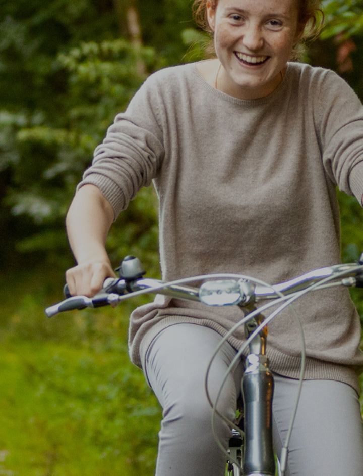 Happy young woman riding her bicycle towards the camera – it’s a bright spring day and everything is looking very green