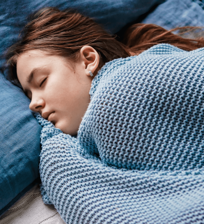 Tired girl snuggled up in a blanket in bed – perhaps she has hay fever symptoms, which can cause disturbed sleep¹