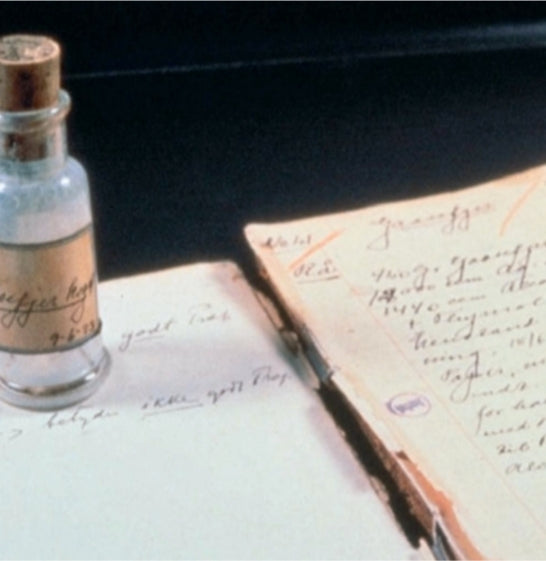An empty apothecary’s bottle and an old-fashioned scientific notebook filled with experiments recorded in pen and ink
